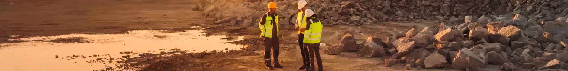 Group of engineers inspecting construction site near rocky shoreline with safety gear and hard hats.