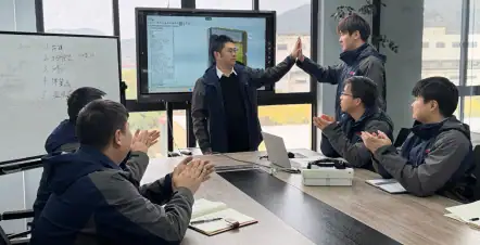 A business meeting with professionals collaborating around a conference table, presenting ideas and working on a digital whiteboard, highlighting teamwork and strategic planning.