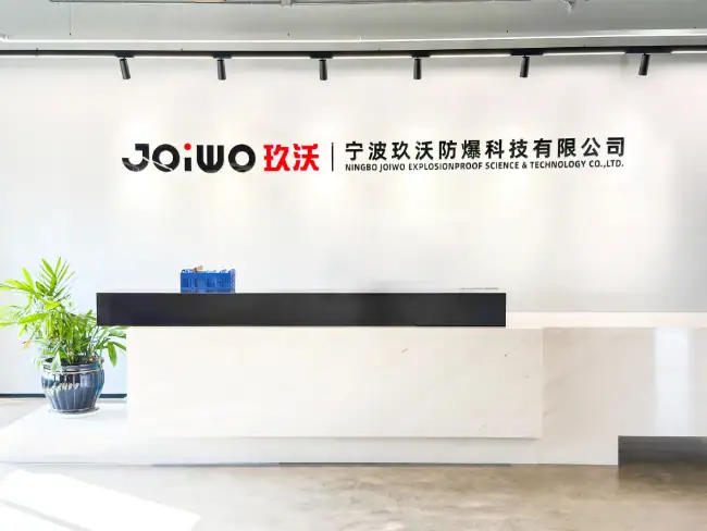 A sleek modern reception desk with the Joiwo logo and Chinese characters, featuring a potted plant and a clean, minimalistic design in a well-lit corporate office environment.
