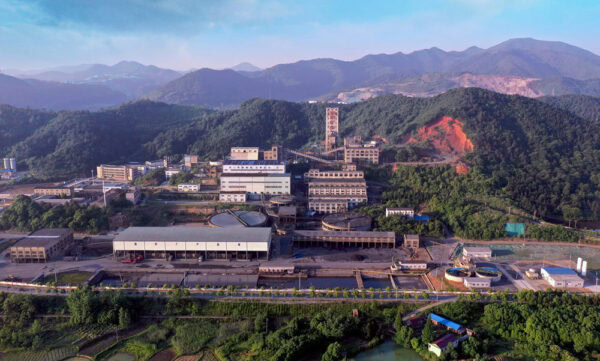 An aerial view of the Tongling Chemical Group Xinqiao Mining Project, showcasing industrial buildings, mining operations, and surrounding mountainous landscape in a lush green environment.