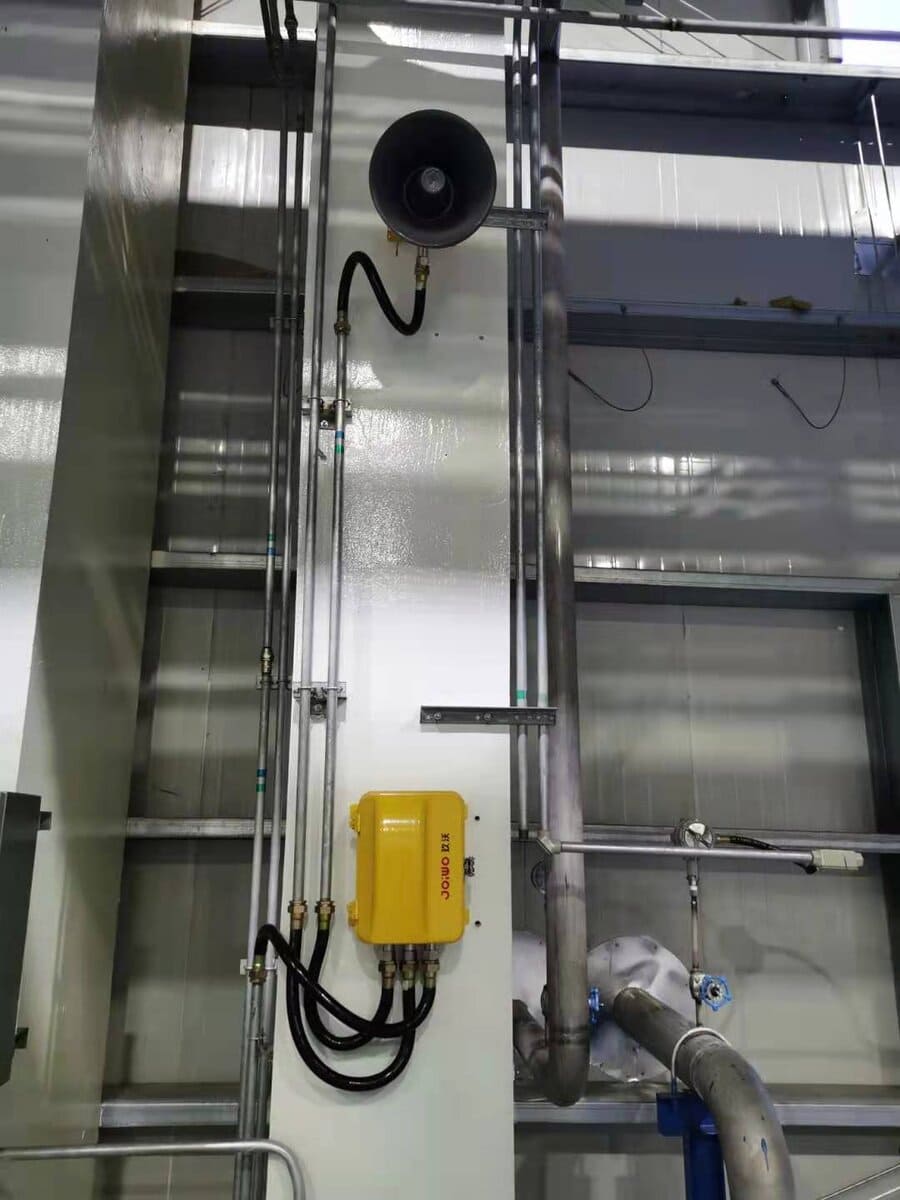 Industrial piping and monitoring equipment at CNOOC Dongying Project site, featuring a loudspeaker, control box, and metal pipes in an industrial setting.
