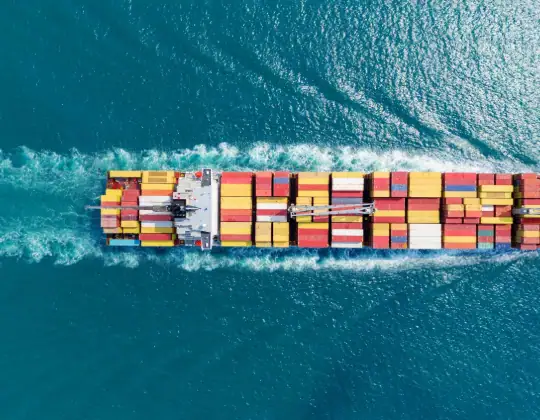 Aerial view of a large container ship sailing through the ocean, carrying multicolored cargo containers, showcasing global shipping and logistics.