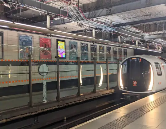 Modern city subway station with sleek train and illuminated advertisements on the platform.