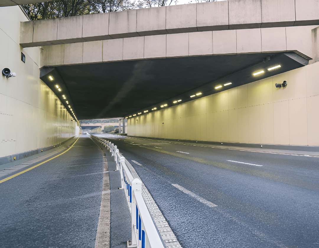 Underpass tunnel with road and safety barriers, illuminated by overhead lights.