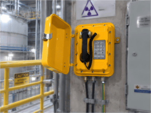 Yellow explosion-proof telephone mounted on industrial wall in nuclear power plant with safety signs and warning labels.