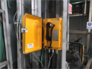 Yellow industrial telephone with keypad and handset in a rugged industrial setting, designed for copper mining operations in Chile.