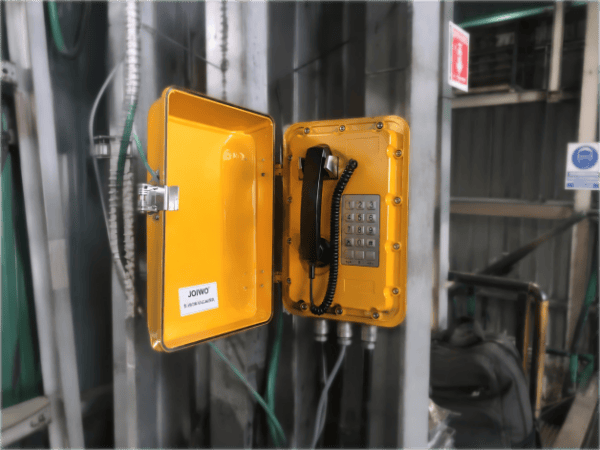 Yellow industrial telephone with keypad and handset in a rugged industrial setting, designed for copper mining operations in Chile.
