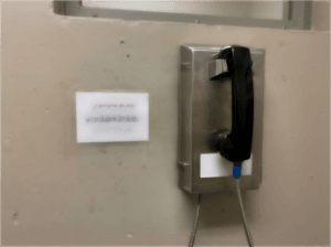 Secure prison telephone mounted on wall with stainless steel panel and black handset, designed for maximum security facilities in South Africa.