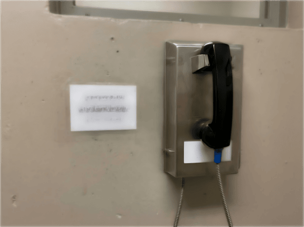 Secure prison telephone mounted on wall with stainless steel panel and black handset, designed for maximum security facilities in South Africa.