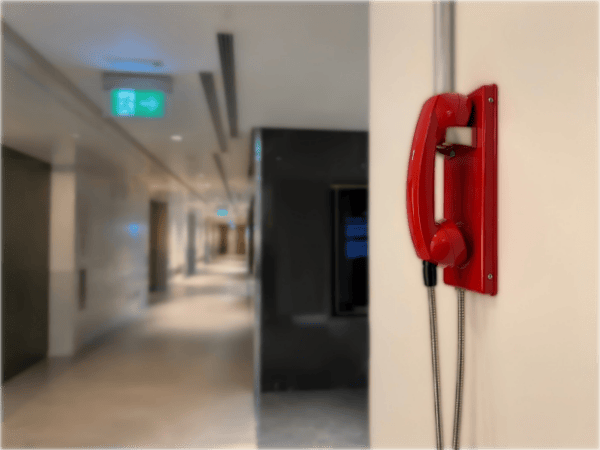 Red fire emergency telephone mounted on a wall in a modern commercial building corridor in the UAE.